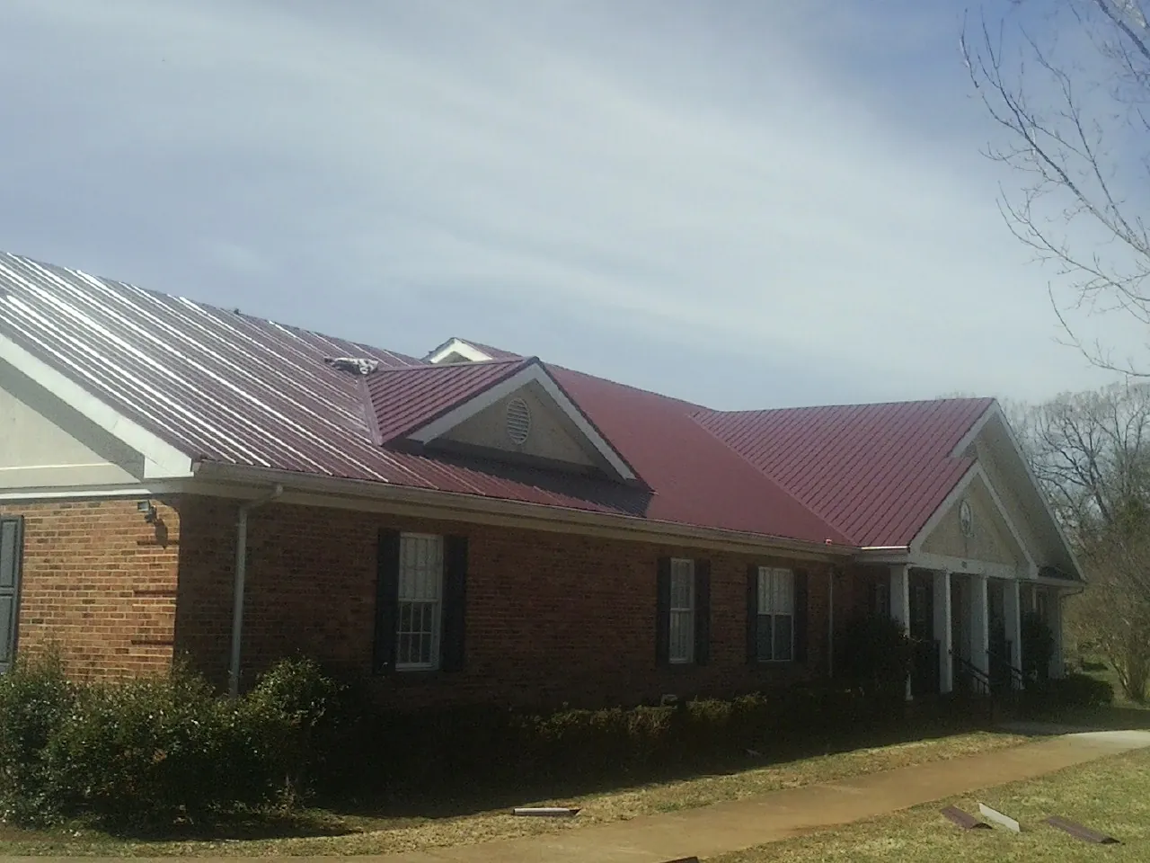 Red metal roof with gabled entries on a long brick building, from a Hail Damage Roof Repair job in Lissie