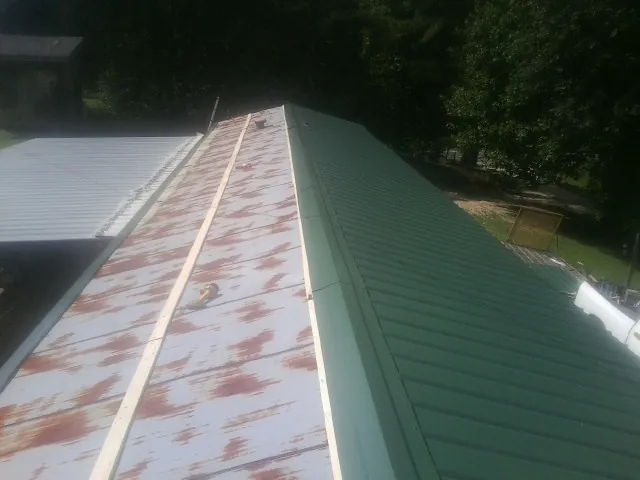 Old rusted panels beside newly installed green metal roofing — Wind Damage Roof Repair by Roofing Brothers in Lissie