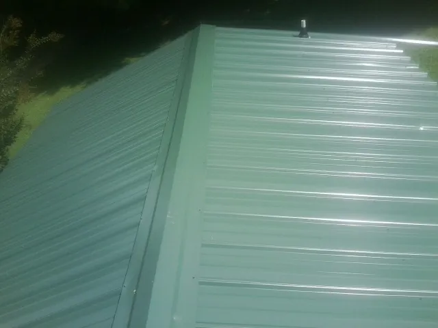 New green metal panels meeting at the ridge of a roof — Flat Roof Repair work by our crew in Lissie