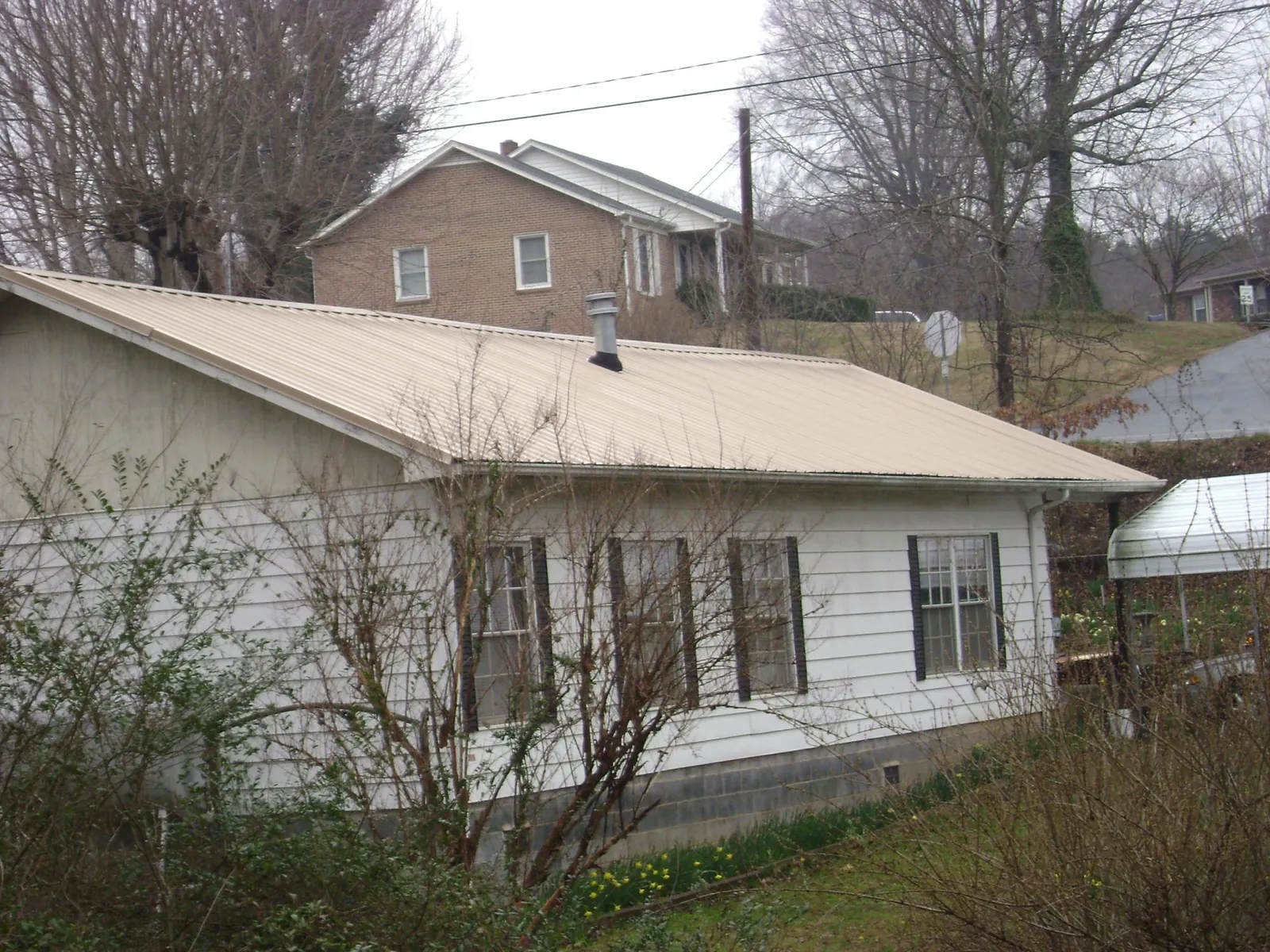 Tan metal roof on a white sided house set into a hillside — Commercial Roofing by Roofing Brothers in Lissie