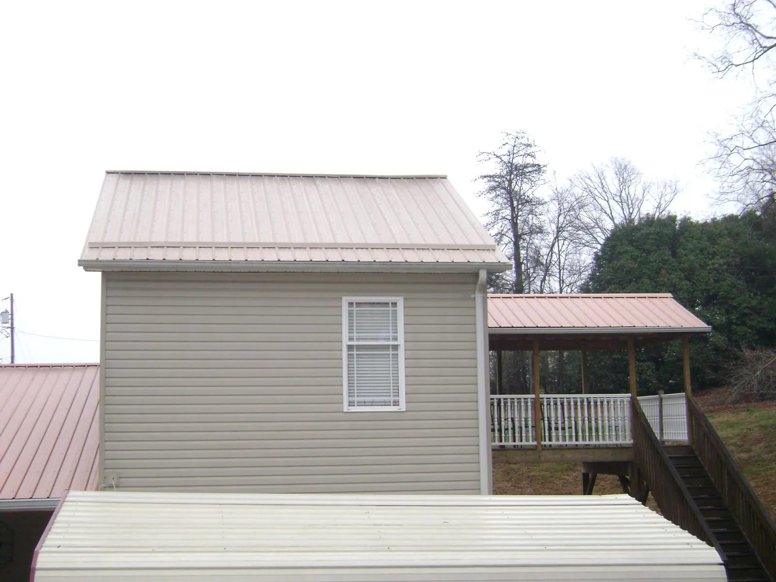 Tan metal roofs on a two story addition and attached porch, from a Roof Replacement job in Lissie